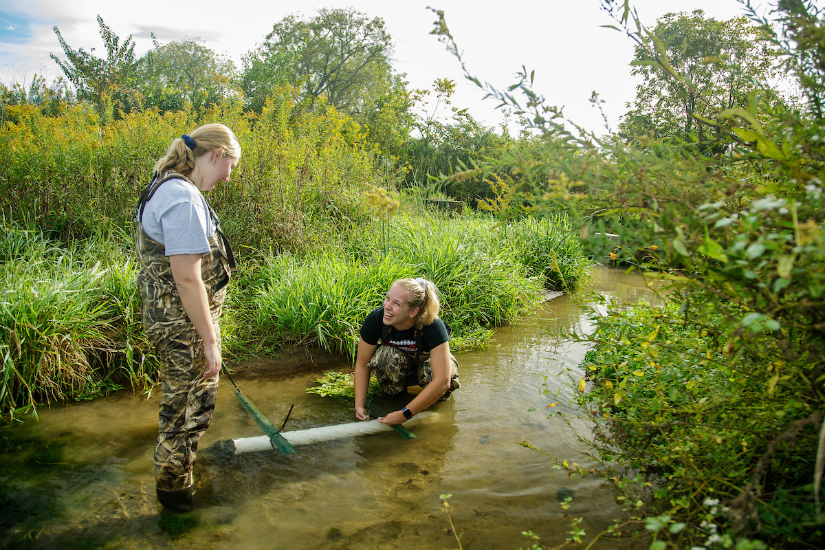 Two female agriculture students collecting water samples from creek