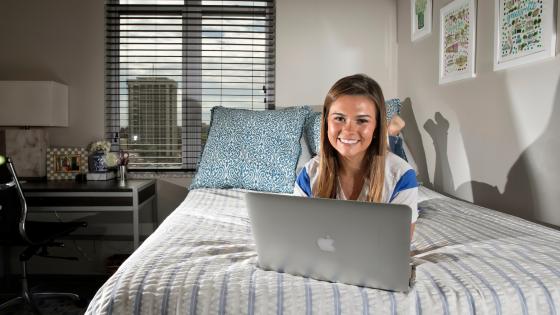 Student with laptop on bed in residence hall