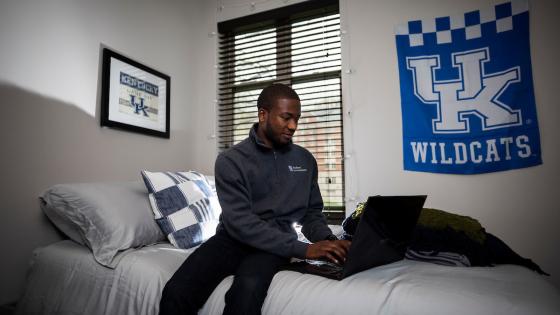 Student sitting on bed with laptop in residence hall