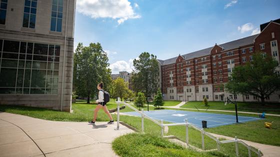 Student walking by basketball court surrounded by Residence Halls