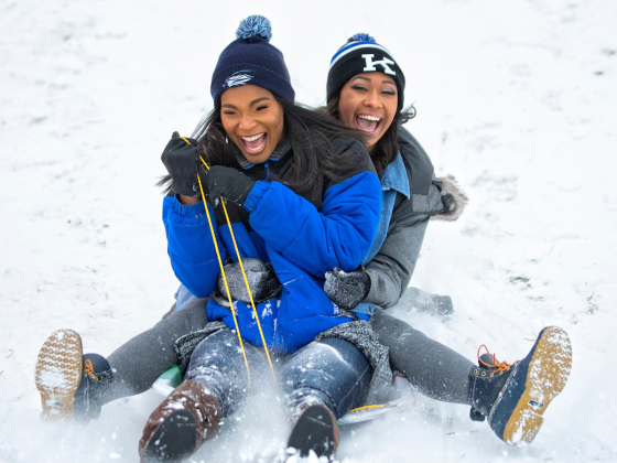 Two students sledding in the snow on campus