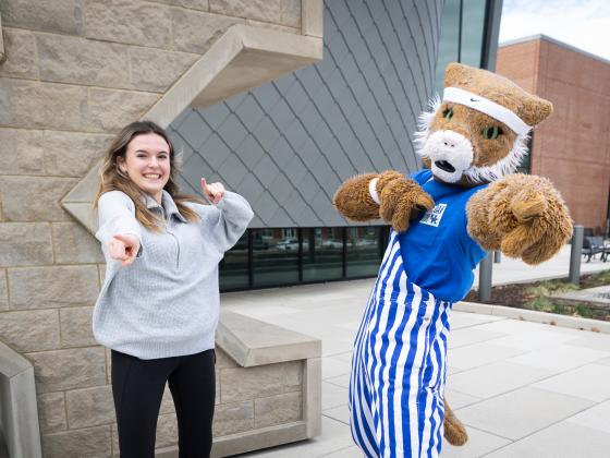 UK student and Wildcat mascot pointing directly at camera