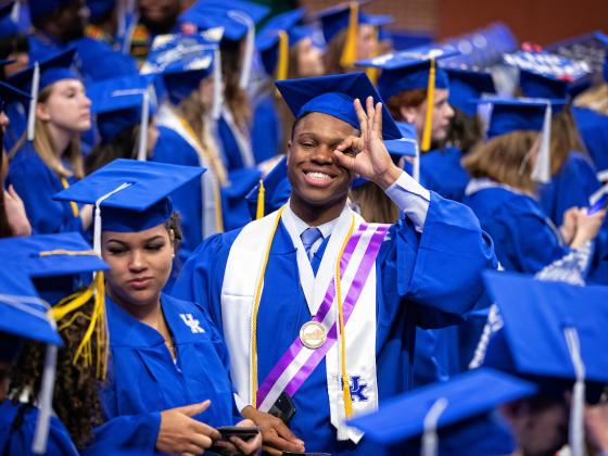 Student in graduation gown and hat making the 3-point shot symbol