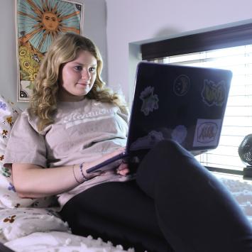 Erin Yates studying on laptop in top bunk of Tri-It space